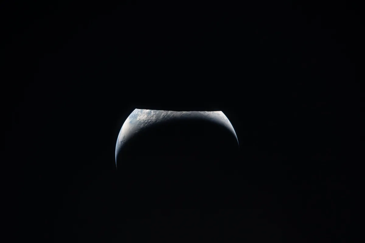 Tierra como creciente sobre el limbo lunar, vista desde la ventana de Orion durante el sobrevuelo de Artemis II